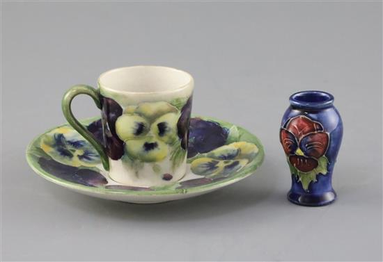 A Moorcroft pansy pattern coffee cup and saucer, c.1915 and a similar later miniature vase, H.5.1cm